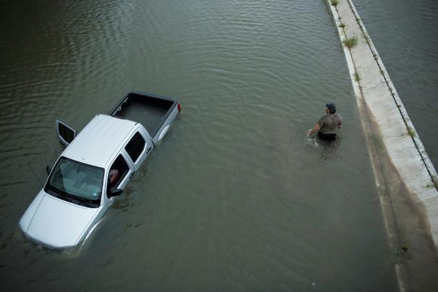 Un américain passe devant une voiture abandonnée alors que les eaux continuent de monter à Houston, le 28 août 2017 [Brendan Smialowski / AFP]