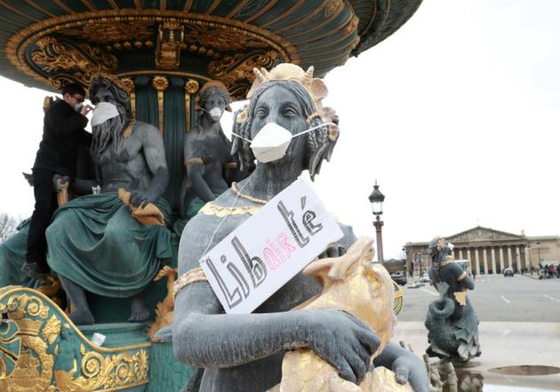 Un militant pose des masques le 31 mars 2018 devant la bouche de statues place de la Concorde, afin de dénoncer l'inaction des pouvoirs publics contre la pollution de l'air [JACQUES DEMARTHON / AFP]