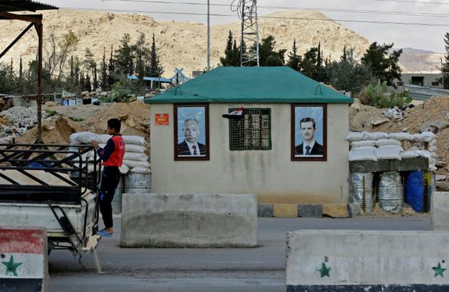 Les portraits de Bachar al-Assad et de Vladimir Poutine suspendus sur un poste de contrôle de Mukhayyam al Wafidin dans la banlieue de Damas non loin de l'enclave rebelle assiégée dans la Ghouta orientale, le 28 février 2018 [LOUAI BESHARA / AFP]