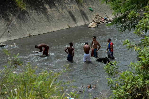 De jeunes Vénézuéliens fouillent toute la journée à mains nues parmi les débris charriés par le courant les eaux sales du fleuve Guaire de Caracas, le 1er février 2018 [FEDERICO PARRA / AFP/Archives]