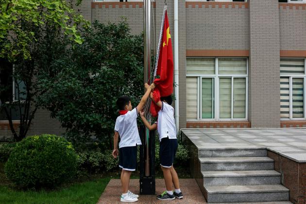 Des écoliers ajustent le drapeau national chinois dans la cour de leur école, à Shanghai, le 27 septembre 2017 [Chandan KHANNA / AFP]