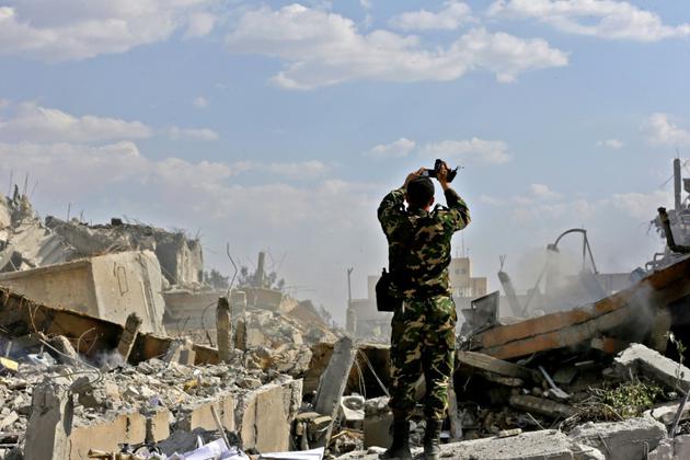 Un soldat syrien photographie les décombres d'un bâtiment faisant partie d'un centre de recherches dans le nord de Damas visé par des frappes américaines, françaises et russes en représailles à une attaque chimique présumée, le 14 avril 2018, lors d'une visite organisée par le ministère syrien de l'Information [LOUAI BESHARA / AFP]