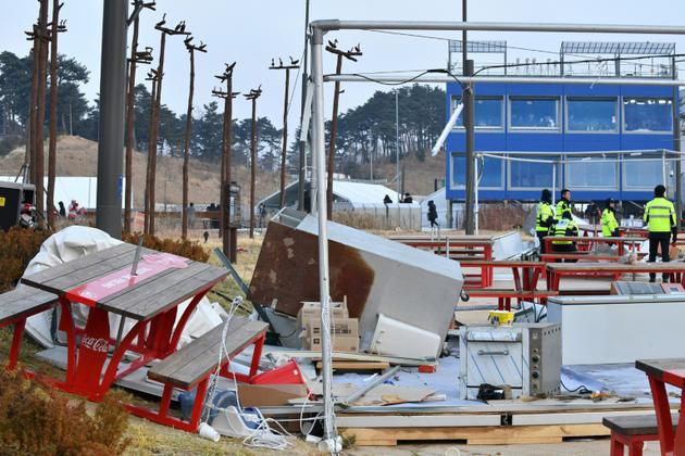 Des policiers près des stands de nourriture qui se sont envolés à cause des vents violents, à l'extérieur de la patinoire Arena de Gangneung, le 14 février 2018 [Mladen ANTONOV / AFP]
