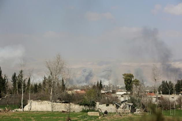 Photo prise depuis les positions des forces du régime syrien montrant de la fumée qui s'élève au-dessus de la ville de Jisrine, dans l'enclave rebelle assiégée de la Ghouta orientale, le 11 mars 2018 [STRINGER / AFP]