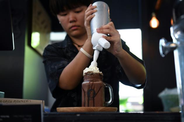 Une employée du Café de prise de conscience de la mort prépare un milkshake au chocolat baptisé "mort", à Bangkok, le 30 mars 2018 [LILLIAN SUWANRUMPHA / AFP]