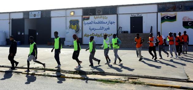 Des migrants camerounais (orange) et Sénégalais (jaune) rejoignent le terrain où ils s'apprêtent à disputer un match de football au camp de Tarjoura en Libye, le 28 février 2018 [MAHMUD TURKIA / AFP]