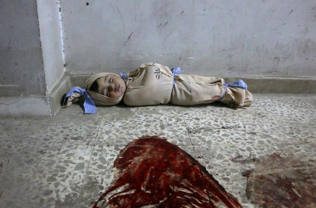 Le corps d'un enfant syrien enveloppé dans une couverture et placé à même le sol dans une clinique de fortune dans la localité de Douma, dans le fief rebelle de la Ghouta orientale, cible de bombardements intensifs du régime, le 22 février 2018 </p>
<p> [Hamza AL-AJWEH / AFP]