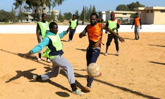 Des migrants Camerounais (orange) et Sénégalais (jaune) participent à un match de football au camp de Tarjoura en Libye, le 28 février 2018 [MAHMUD TURKIA / AFP]