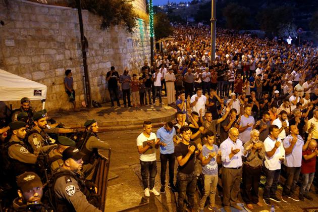 Des forces de sécurité israéliennes regardent des palestiniens prier à l'extérieur de l'esplanade des Mosquées à Jérusalem le 24 juillet 2017 [Ahmad GHARABLI / AFP]