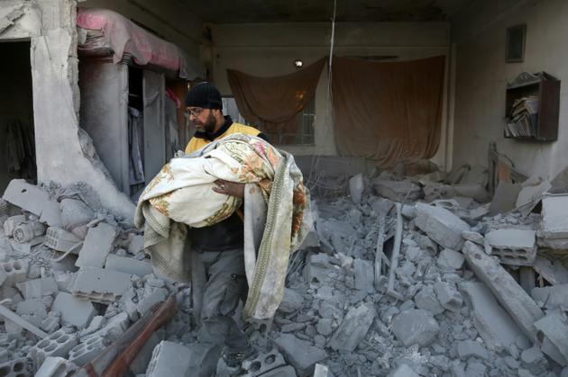 Un membre de la Defense civile porte le corps d'un enfant, retrouvé dans les décombres d'un bâtiment touché par des raids du régime dans la ville rebelle de Jisrine, à l'est de Damas le 8 février 2018 [ABDULMONAM EASSA / AFP]
