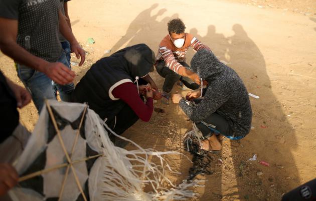 Des Palestiniens tentent d'attacher un cocktail Molotov à un cerf-volant qu'ils comptent faire s'envoler au-dessus de la frontière entre la bande de Gaza et Israël, le 18 avril 2018 [MAHMUD HAMS / AFP]